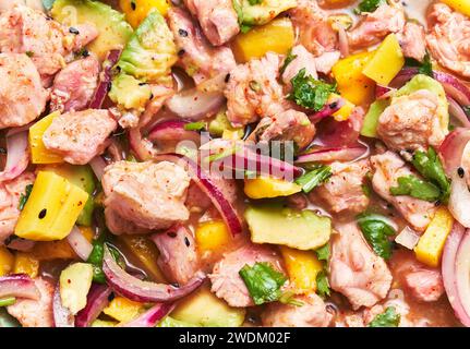 Gros plan d'un plat de ceviche vibrant avec du saumon, de l'avocat, de la mangue, de la coriandre et des oignons sur un fond flou. Banque D'Images