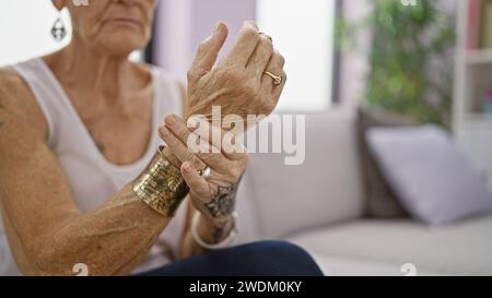 Femme âgée aux cheveux gris courts, souffrant de douleurs au poignet, assise sur un canapé à la maison Banque D'Images