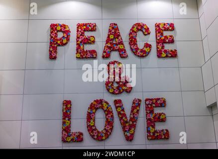 Vue des mots décoratifs « Peace and Love » fabriqués avec des fleurs rouges artificielles sur un mur carrelé blanc. Banque D'Images