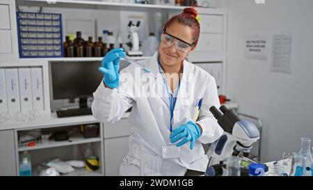 Brillante jeune femme rousse scientifique engrosée dans la recherche médicale, mesurant méticuleusement le liquide dans un tube à essai, gants de sécurité sur, à la h occupé Banque D'Images