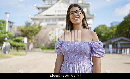 Joyeuse beauté latine en lunettes, une femme brune pose avec un sourire confiant et insouciant au célèbre château d'osaka, débordant de joie et de bonheur Banque D'Images