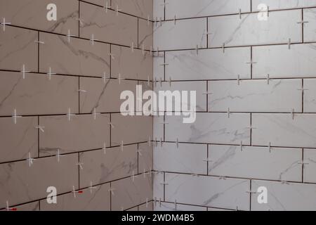 Carrelage mural rectangulaire nouvellement appliqué dans une cabine de douche avec les entretoises en plastique Banque D'Images