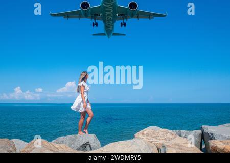 Rencontre côtière : fille en robe blanche sur pierres, avion annonçant de la mer Bleue Banque D'Images