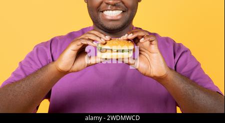 Cliché recadré de Black Guy tenant Burger sur fond jaune Banque D'Images