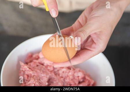 Les mains d'une femme ont battu un œuf en viande, gros plan. Le processus de cuisson de la viande. Banque D'Images