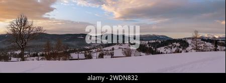 Petit village alpin et hiver montagne enneigée au premier lever du soleil autour, Voronenko, Carpates, Ukraine. Tracer sur un chemin fraîchement trodden à travers g Banque D'Images