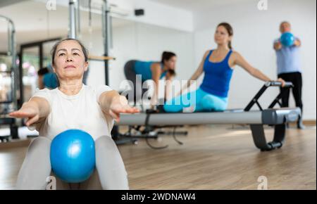Femme âgée qui fait des sit-ups avec le ballon pendant l'entraînement de pilates Banque D'Images