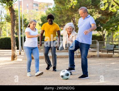 Joyeux amis multinationaux jouant au football sur un terrain de jeu sablonneux lors d'une chaude soirée de printemps Banque D'Images
