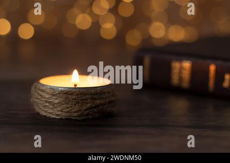 Bougie brûlant avec flamme vive et livre sacré fermé de la bible sur la table en bois avec fond de bokeh. Gros plan. Lumière spirituelle qui brille dans les ténèbres. Banque D'Images