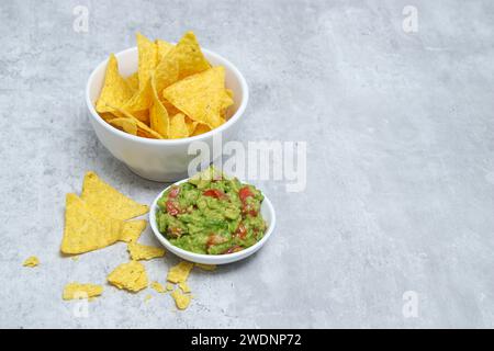 Vue de dessus de chips tortilla dans un bol blanc et guacamole à l'avocat sur une table grise Banque D'Images