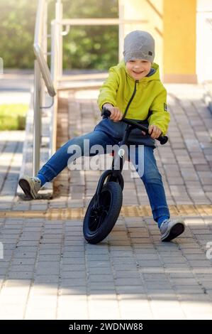 Petit enfant s'amusant sur vélo d'équilibre en ville, en plein air. Il descend la pente et apprend à équilibrer. Banque D'Images