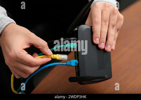 Homme insérant le câble dans le routeur Wi-Fi à la table en bois à l'intérieur, gros plan Banque D'Images