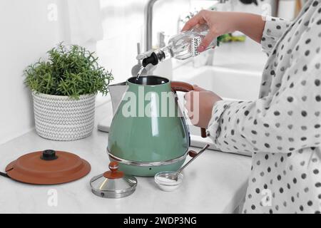 Femme versant du vinaigre de bouteille dans une bouilloire électrique dans la cuisine, gros plan Banque D'Images