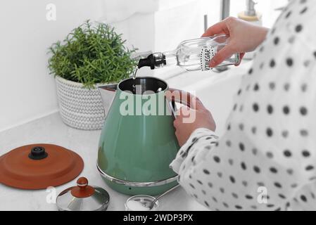 Femme versant du vinaigre de bouteille dans une bouilloire électrique dans la cuisine, gros plan Banque D'Images