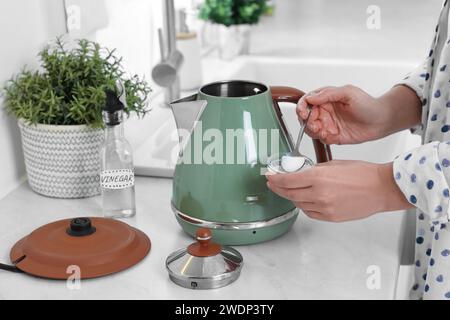 Femme ajoutant du bicarbonate de soude dans une bouilloire électrique dans la cuisine, closeup Banque D'Images