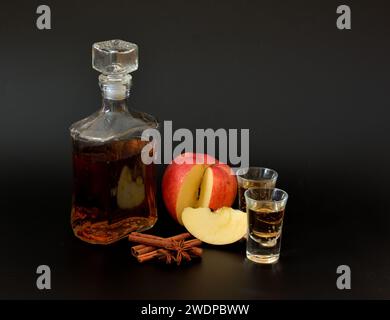 Liqueur de pomme avec cannelle, anis et tranches de pomme mûres sur fond noir dans une bouteille et deux verres. Gros plan. Banque D'Images