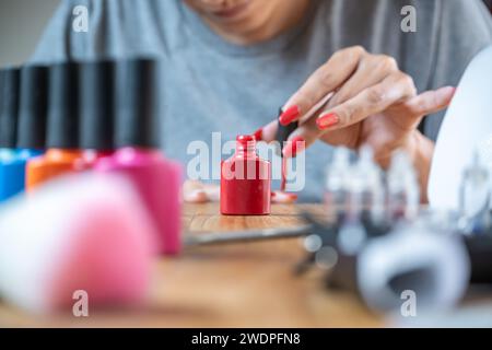 Jeune femme appliquant un vernis à ongles rouge semi-permanent. Photo avec mise au point sur la bouteille rouge de vernis à ongles. Banque D'Images
