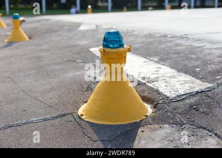 Gros plan d'un marqueur de piste jaune avec un feu bleu, indiquant les directions sur le tarmac de l'aéroport Banque D'Images