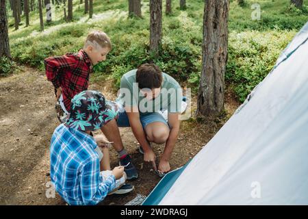 homme caucasien érigeant une tente dans une forêt de pins. des enfants l'aident. Concept de camping familial. Photo de haute qualité Banque D'Images