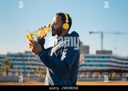 Homme coureur buvant de l'eau d'une bouteille de sport à l'extérieur. Banque D'Images