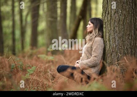 Une jeune femme appuyée sur un arbre dans une forêt luxuriante Banque D'Images