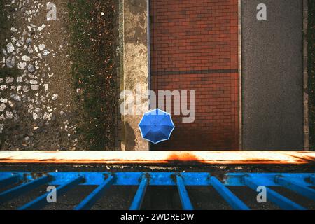 Vue de dessus de la personne avec parapluie bleu marchant dans la rue pavée un jour de pluie, directement au-dessus Banque D'Images