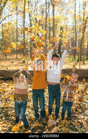 Frères et sœurs heureux jetant des feuilles jaunes d'automne ensemble dans la forêt ensoleillée Banque D'Images