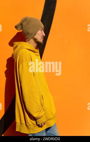 Un gars élégant dans un sweat à capuche jaune se tient de profil contre un jaune Banque D'Images