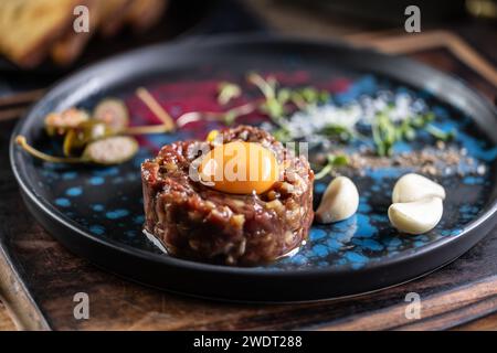 Tartare de boeuf avec jaune d'oeuf sur une assiette avec de l'ail et du pain grillé. Banque D'Images