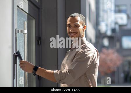 Joyeux jeune homme d'affaires afro-américain entrant dans l'immeuble de bureaux, exsudant la confiance avec une carte d'identité en main. Banque D'Images