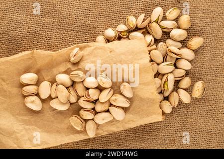 Petite quantité de délicieuses pistaches avec sac en papier sur toile de jute, macro, vue de dessus. Banque D'Images