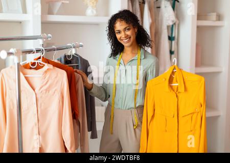 Créateur de mode souriant avec des vêtements sur rack Banque D'Images