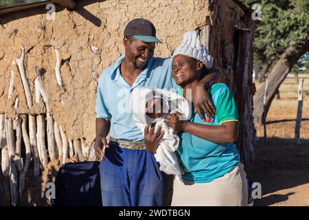 Joyeux parents africains tenant leur nouveau-né, maison de boue dans le village d'arrière-plan au Botswana Banque D'Images