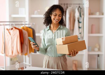 Entrepreneur souriant avec des colis et téléphone à la boutique de mode Banque D'Images