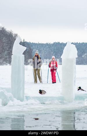 Mère et fille randonnant ensemble sur un lac gelé avec forêt sur fond en hiver en Lituanie, verticale Banque D'Images