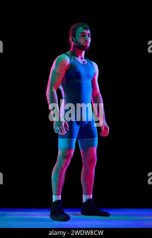 Portrait en longueur d'homme sportif en uniforme de combat bleu posant sur fond noir dans des lumières de néon mixtes. Banque D'Images