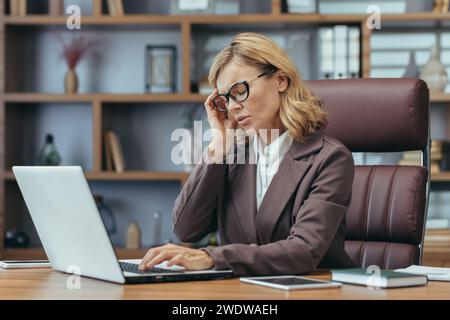 Élégante femme d'affaires mature se concentrant comme elle travaille sur un ordinateur portable d'un bureau à domicile bien aménagé avec un décor de bon goût. Banque D'Images