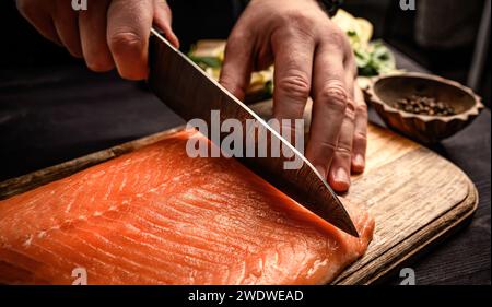 Le chef sushi coupe le saumon cru avec un couteau sur une table en bois pour les sashimis japonais. Cuisinier professionnel préparant la truite fraîche de poisson orange Banque D'Images