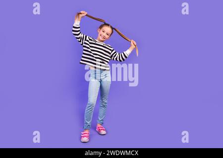 Photo pleine longueur de joli charmant petit enfant porter un pull rayé tenant des queues espace vide isolé fond de couleur violette Banque D'Images