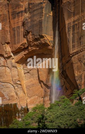 Petite cascade devant une paroi rocheuse rouge est illuminée par le soleil et brille dans des couleurs arc-en-ciel. Banque D'Images