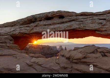 Le soleil brille à travers la Mesa Arch au lever du soleil. Banque D'Images