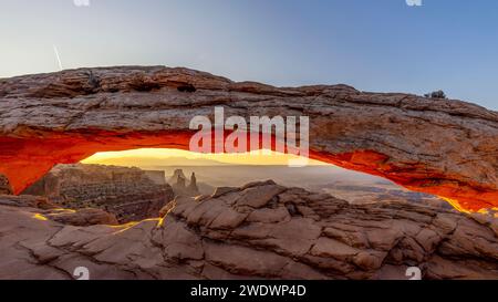 Mesa Arch dans le parc national de Canyonlands est illuminé en orange par le soleil d'en bas au lever du soleil. Banque D'Images