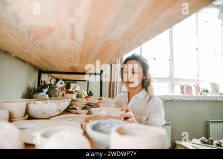 Jeune femme gestionnaire de l'atelier de poterie arrange les produits sur l'étagère Banque D'Images