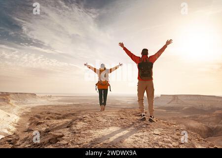 Deux jeunes randonneurs avec des sacs à dos sont debout les bras ouverts contre la vallée et profite du coucher du soleil Banque D'Images