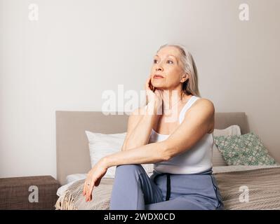Femme âgée frustrée assise sur un lit dans le salon Banque D'Images