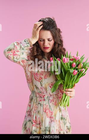 femme moderne stressée avec de longs cheveux bruns ondulés avec bouquet de tulipes sur fond rose. Banque D'Images