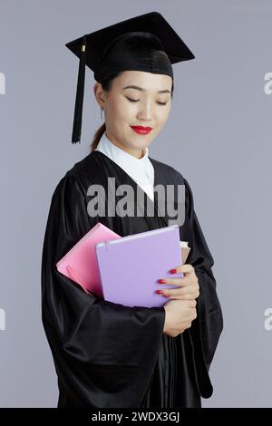 pensive étudiant diplômé moderne femme asiatique avec des livres et des cahiers isolés sur fond gris. Banque D'Images