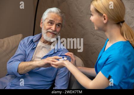 Infirmière vérifiant le pouls ou le niveau d'oxygène à l'aide d'un oxymètre d'homme âgé. Banque D'Images