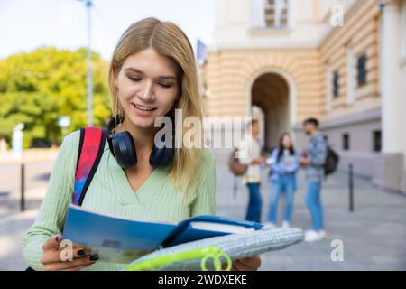 Femme étudiante avec des livres préparant des classes posant en plein air près du collège. Banque D'Images