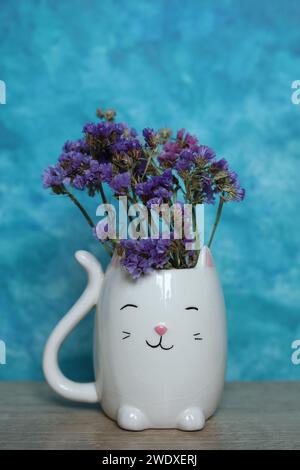 Un bouquet de fleurs séchées dans un vase de chat blanc sur fond bleu Banque D'Images